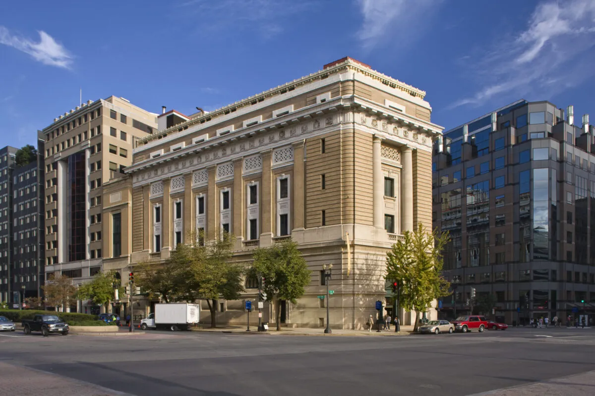 View of the museum from outside showing the Neoclassical building from one corner. The building is a tan-colored stone with an arched doorway, long vertical windows, and detailed molding around the roof.