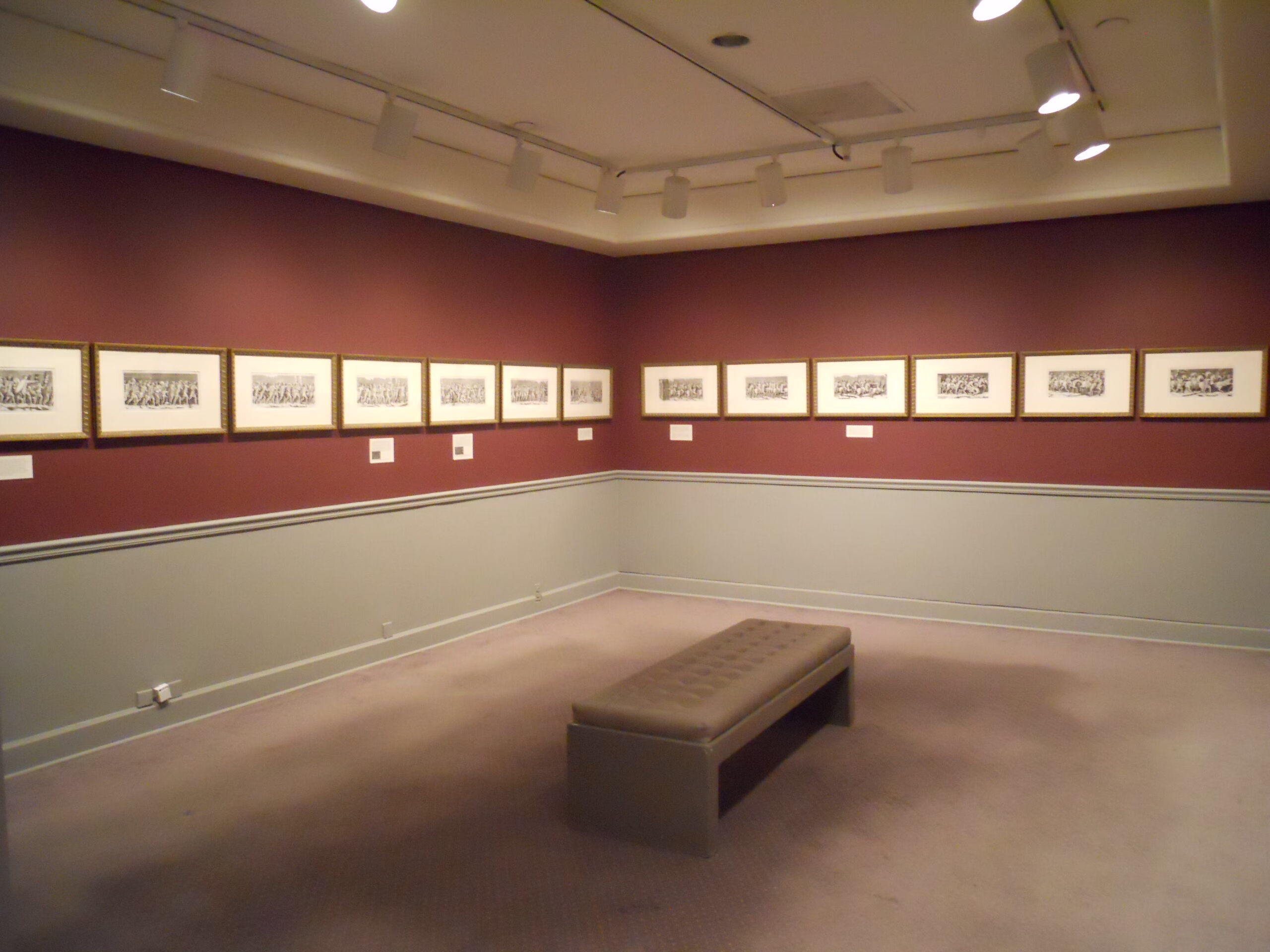 A view of a gallery featuring red walls and a series of black-and-white etchings.