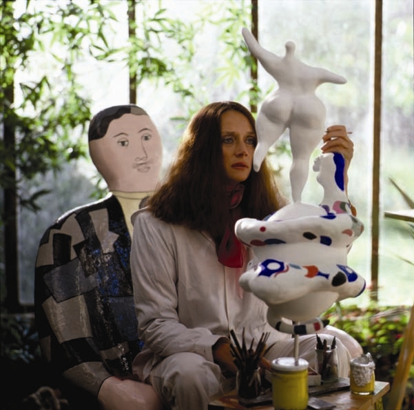 Niki de Saint Phalle sitting in a white jumpsuit painting the sculpture of a 'nana'. 