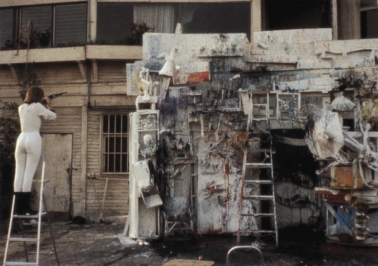 Niki de Saint Phalle photographs a piece of her work that is a combination of found objects mounted to a building.