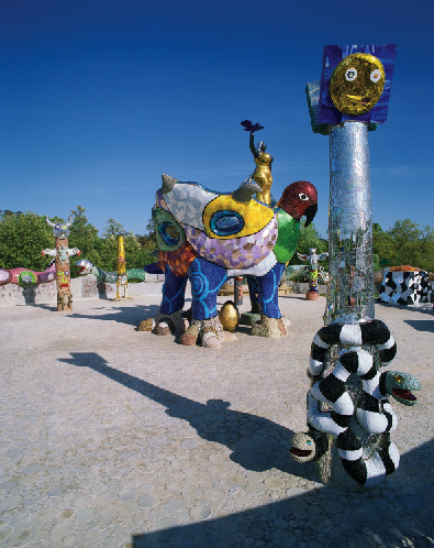 A sculpture of a flower with eyes and a mouth and a snake wrapped around the stem and a large four-legged bird with the figure of a woman on top of it. 