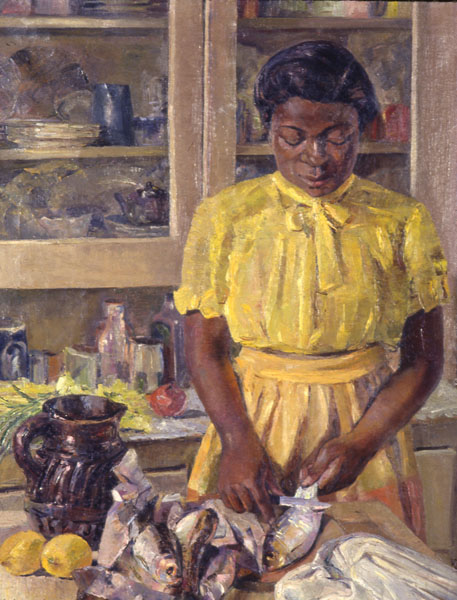 A dark-skinned woman wearing a yellow blouse and skirt is descaling fish with a knife. Amongst the fish on the table are two lemons and a deep amber colored jug. Behind the woman on a counter is more produce and shelves of dishware.