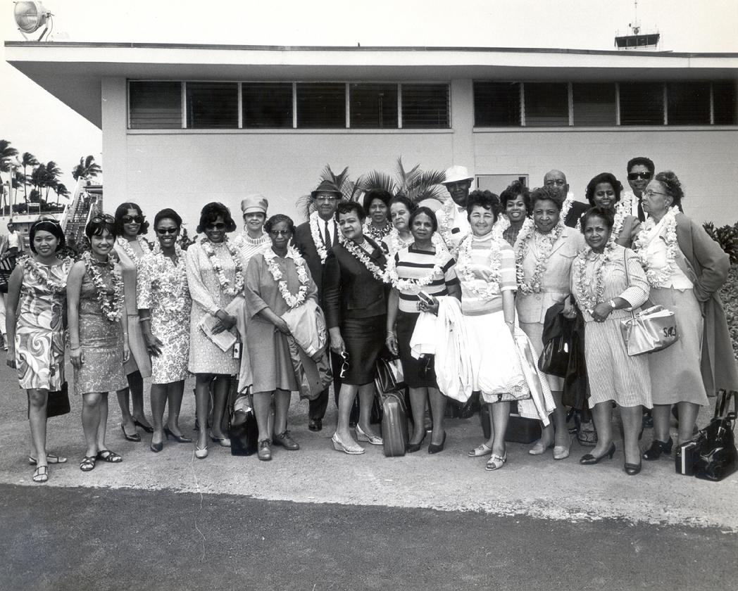 A black and white photograph of a group of people standing together wearing leis.