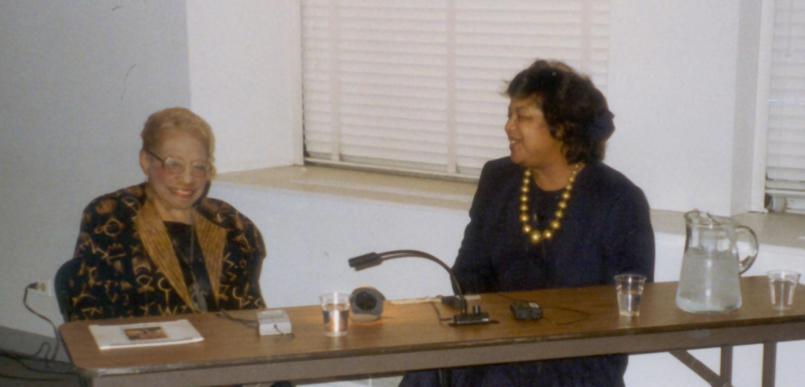 Two women sitting together at a brown table.