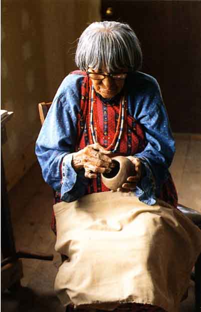 A woman with a light medium tone and gray hair is shaping a ceramic bowl.
