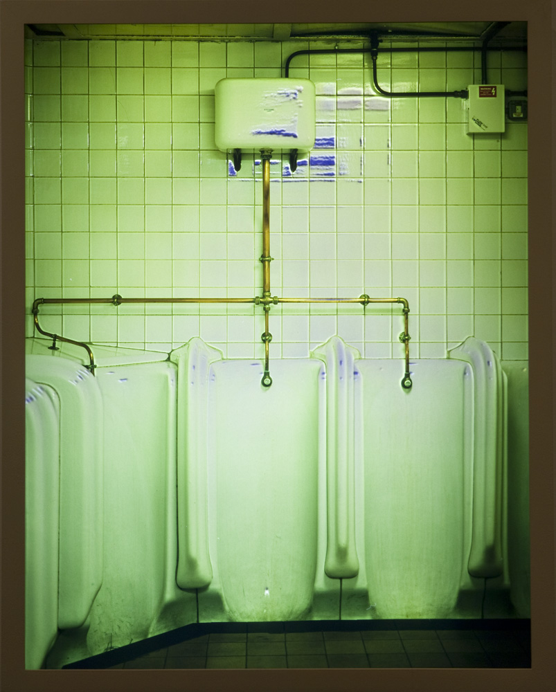 A photograph of the interior of a bathroom showing several urinals. The photograph is tinted in green.