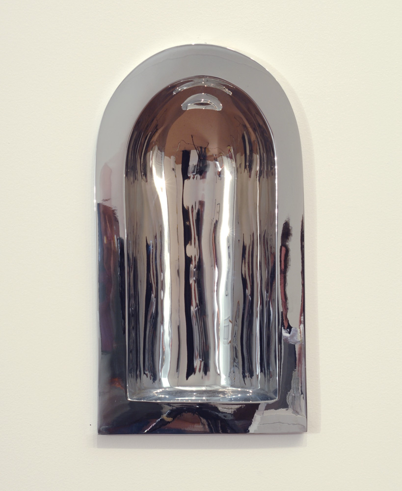 A chrome sculpture attached to a wall, resembling a warped mirror.