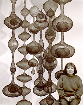 A a Japanese woman sitting next to a sculpture of wavy shapes.