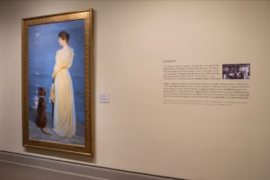 A painting of a woman standing by a beach hanging on a wall.