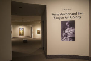 View of a gallery space. On a white wall, it says "A World Apart: Anna Ancher and the Skagen Art Colony."