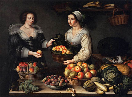 Two women are standing by a table with fruit and vegetables.