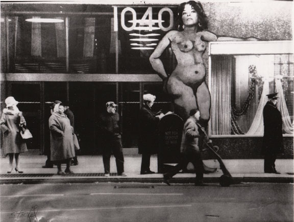 People waiting for a bus before a large sign of a naked woman.