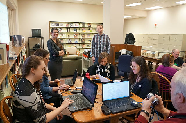 A group of people sitting on their laptops around a table in a library.