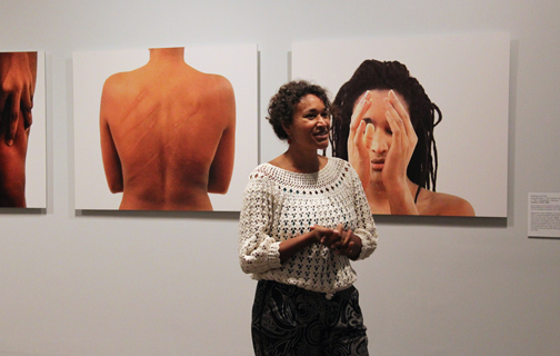 A woman with a medium-dark skin tone is standing before a photo series showing different body parts of a woman.