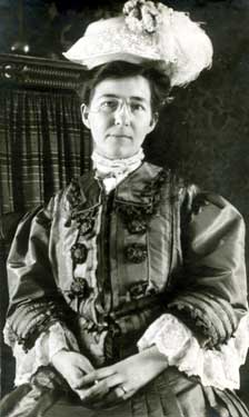 A portrait photograph of a woman in a dress and a big white hat.