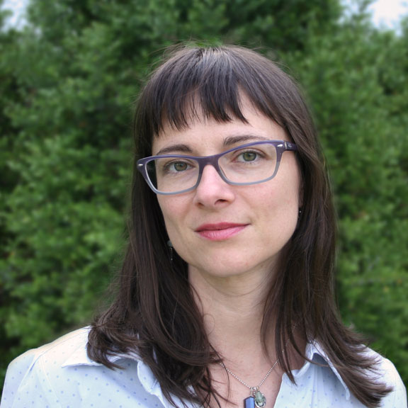 A portrait photograph of a woman with a light skin tone with brown hair wearing glasses.