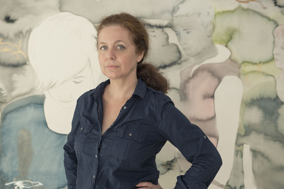 Portrait photograph of a woman with a light skin tone standing in front of a painting.