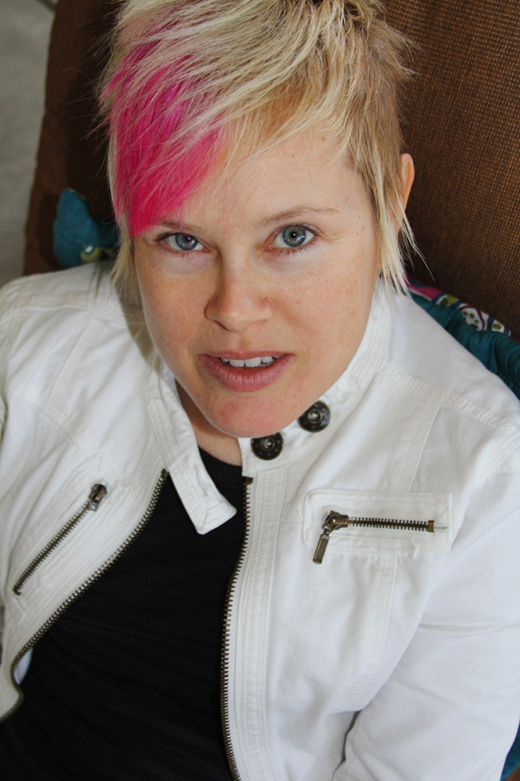 Portrait of a woman with a light skin tone and short, blonde hair with a pink streak.