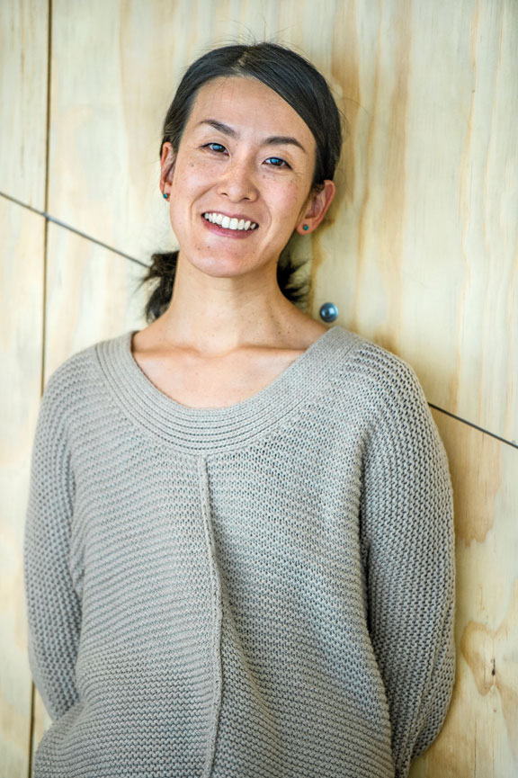 Portrait photograph of an Asian woman standing in front of a beige wall.