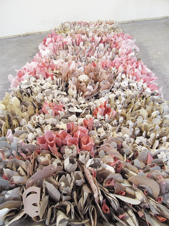 A bed of flowers made out of paper and clay assembled on the floor of a gallery.