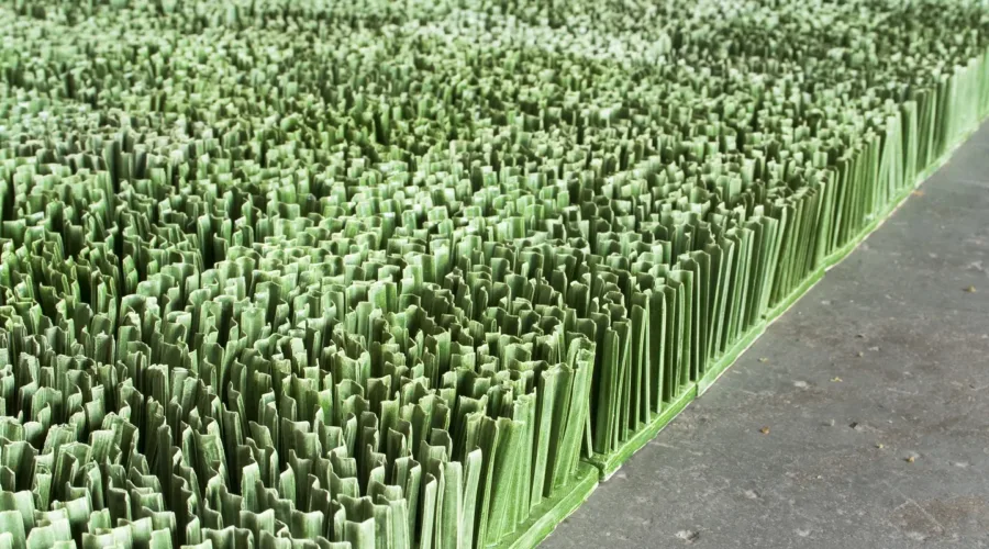 Detail photograph of ceramic sculpture made to look like a patch of lawn. Individual squares consisting of multiple upright blades of porcelain grass, glazed green, fit together to form a lush rectangular field of grass.