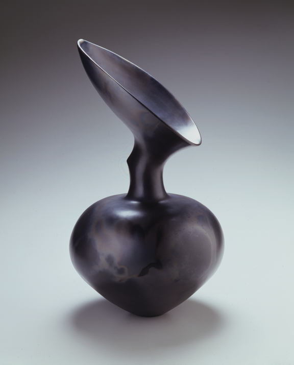 A ceramic vase in the shape of an apple with a leaf. It is black and has a shiny surface. Its shape makes it look otherworldly.