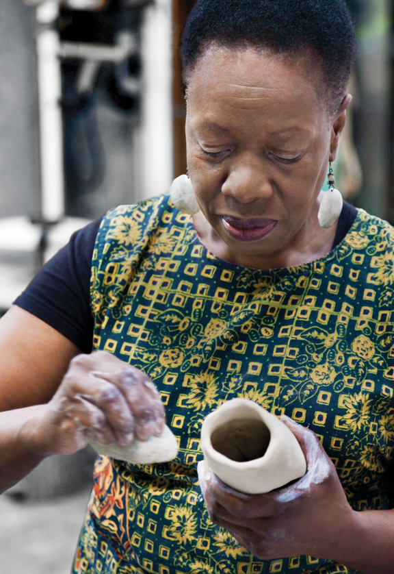 A woman with a dark skin is working on a ceramic vase.