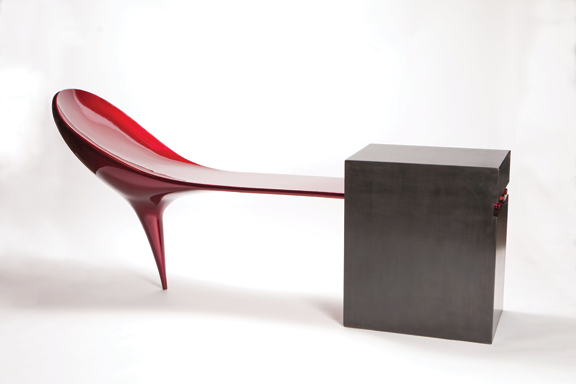 A sculpture made out of two pieces, the left piece is red and the right is a black block. The red piece is attached to the block. It resembles the heel of a red high heel.