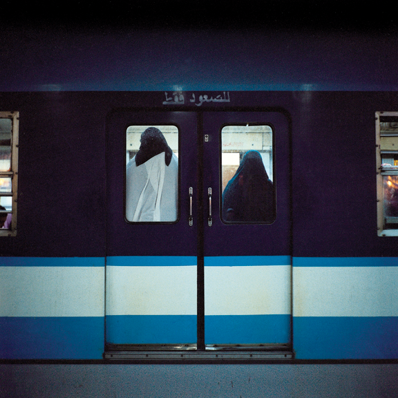 A photograph of a metro cart. In the windows, we can see the silhouettes of two people in black hijabs. 