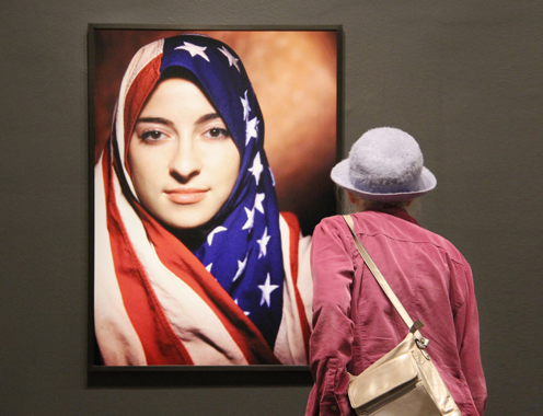 A NMWA visitor studies Boushra Almutawakel’s art work featuring a woman wearing a hijab with a print of the flag of the United States.