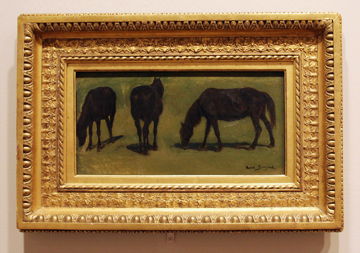 Three black horses are grazing in a meadow. The painting is framed in a thick, golden frame.