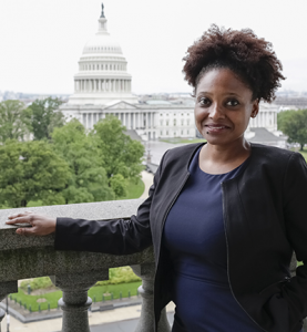 A woman with a dark skin tone standing before the capitol.