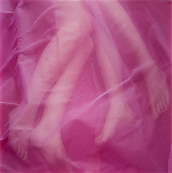 Two pairs of light-skinned legs and feet veiled by a gauzy pink fabric.