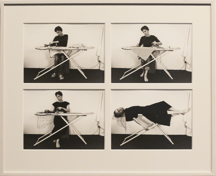 Four framed black-and-white photographs of a light-skinned, dark-haired woman sitting at an ironing board in a seemingly empty interior. Each photograph shows her ironing different items except for the fourth picture in which she lies on top of the ironing board with one arm hanging off the edge.