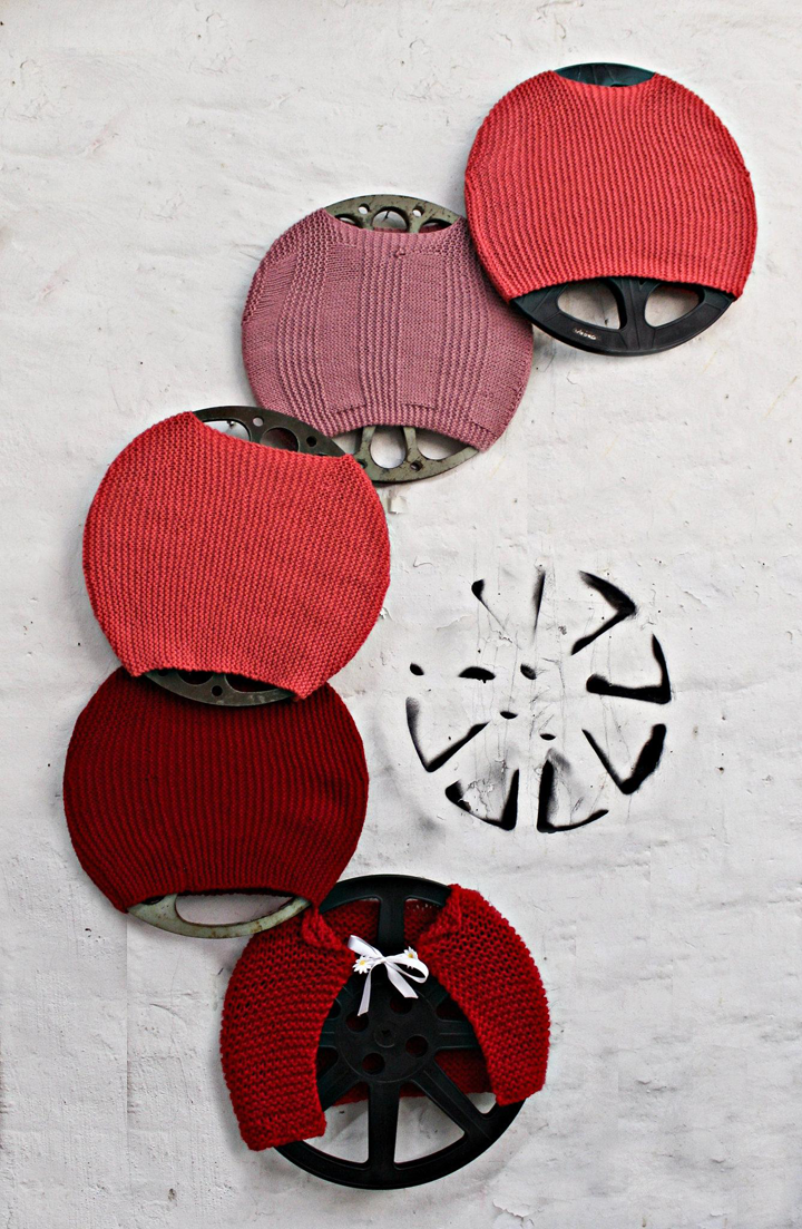 Five film reels wrapped in red wool jersey placed onto a white background.