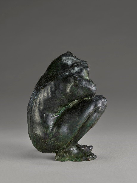 A bronze sculpture of a person sitting on the floor hunched over. The sculpture has a green tone and a worn-in patina. The spine and ribcage are very accentuated, highlighting the thinness of the person.