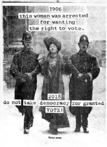 A black-and-white photograph of a woman being escorted by two police men. The police men are holding the women's hands and are wearing custodian helmets. They all have a light skin tone. The text "1906 this woman was arrested for wanting the right to vote. 2018 do not take democracy for granted. VOTE!" is written on the photograph.