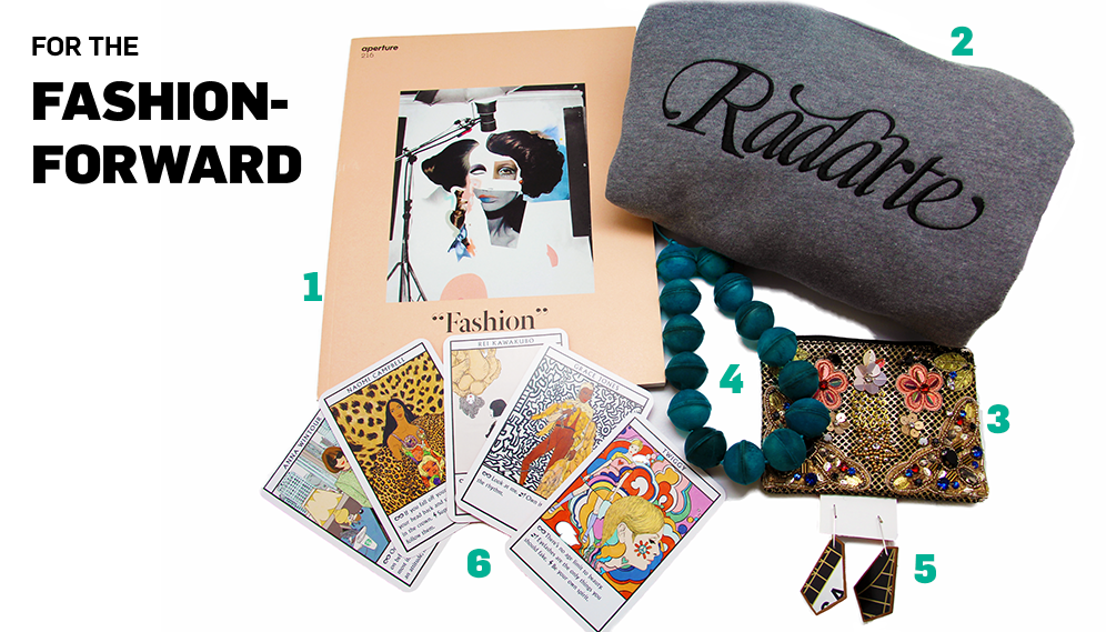 A photograph consisting of six objects arranged against a white background. The objects are a grey sweatshirt with the word "Rodarte" embroidered on it, an issue of Aperture magazine titled "Fashion," a green beaded necklace, select cards from the Fashion Oracles Card Deck, a pair of black and white geometric earrings, and a beaded and embroidered pouch with imagery of flowers and winged creatures. 