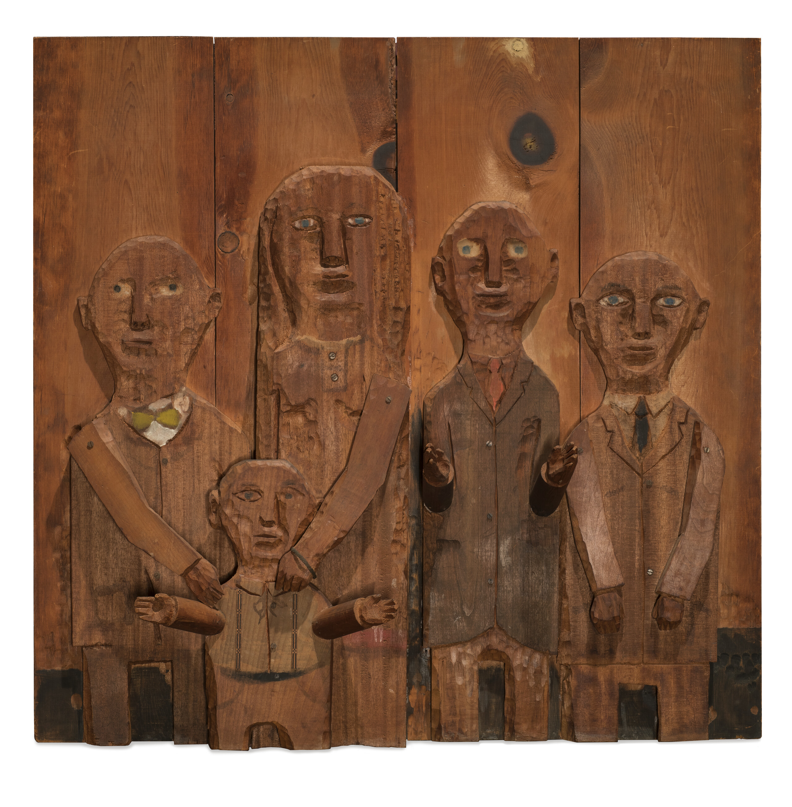 A wooden relief sculpture of four adults and one child. The two figures on the left put their hands on the shoulders of the child in front of them. The arms and hands of all figures are three dimensional and protrude from the work.