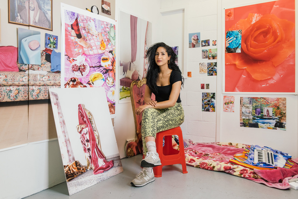 Artist Farah Al Qasimi sits in her studio in Williamsburg, Brooklyn, surrounded by her photographs from her home country, the United Arab Emirates. The photos are vibrant and colorful.