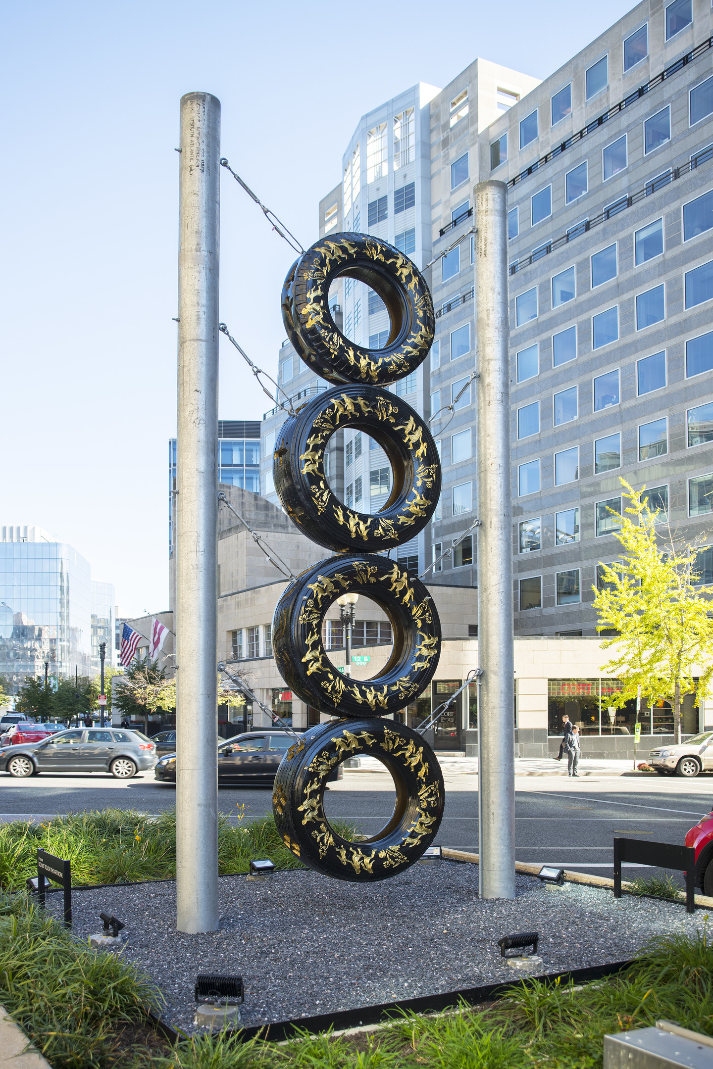 View of New York Avenue showing a tall, totem-like sculpture made of four stacked truck tires with gold leaf embellishments and supported by two steel poles.