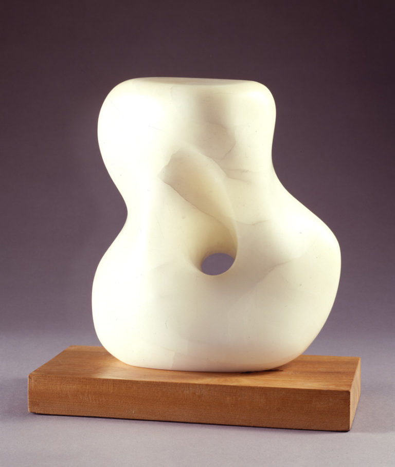 Abstract white stone sculpture, set on a light wood base, smooth and soft, it resembles a woman's twisting torso with a large, rounded hole through the middle.
