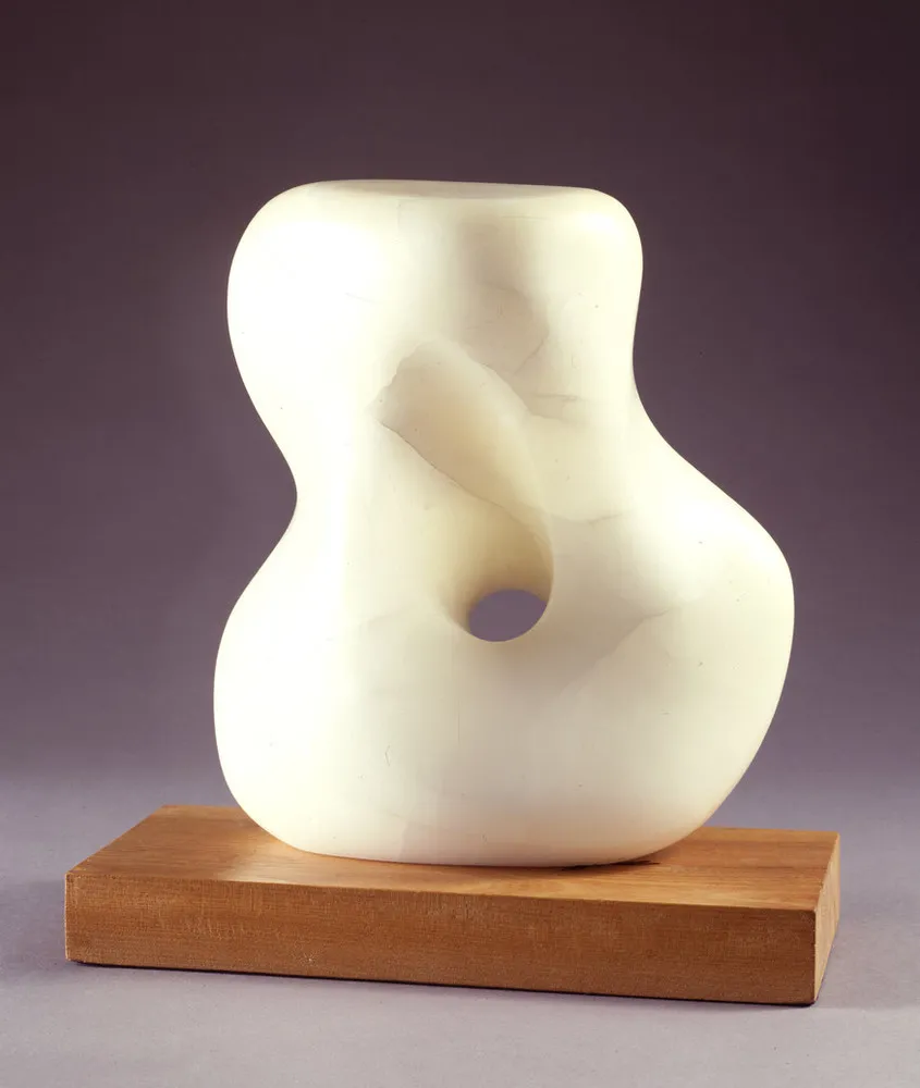 Abstract white stone sculpture, set on a light wood base, smooth and soft, it resembles a woman's twisting torso with a large, rounded hole through the middle.