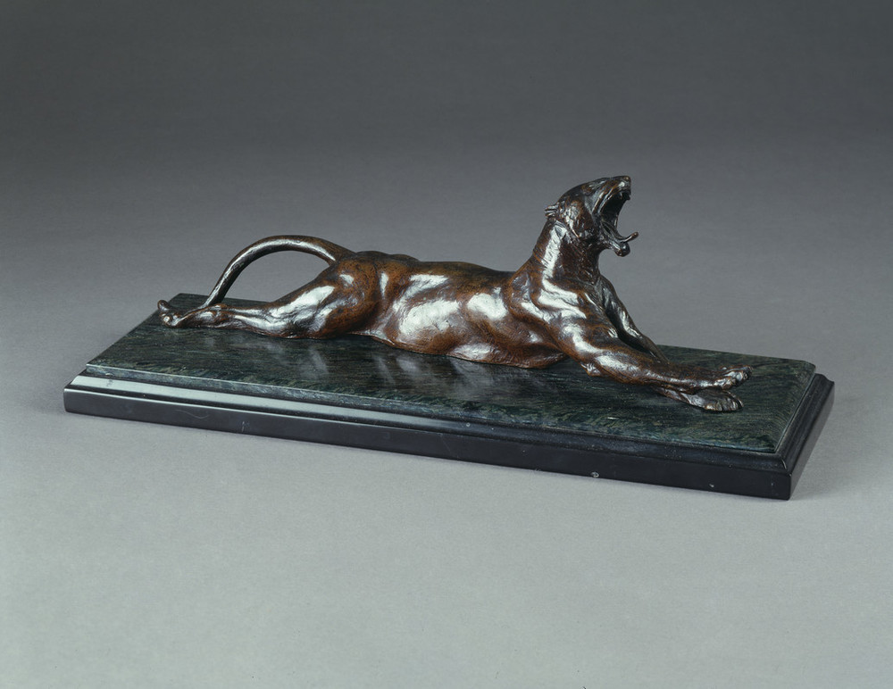 Bronze sculpture set on a polished green-gray stone base depicts a muscular panther with arched back and tail. The animal lies on its belly and stretches front and back legs out while opening its jaw in a convincing yawn, tongue protruding and teeth bared.