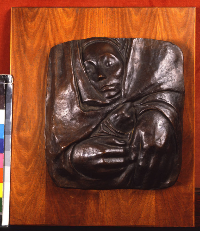 A small face, hands and the suggestion of shoulders form a square bronze relief with rounded corners. The face, on top, looks slightly right, as a pair of hands gather the fabric towards the lower left corner. The fabric folds and creases, forming almost a swirl into the center.
