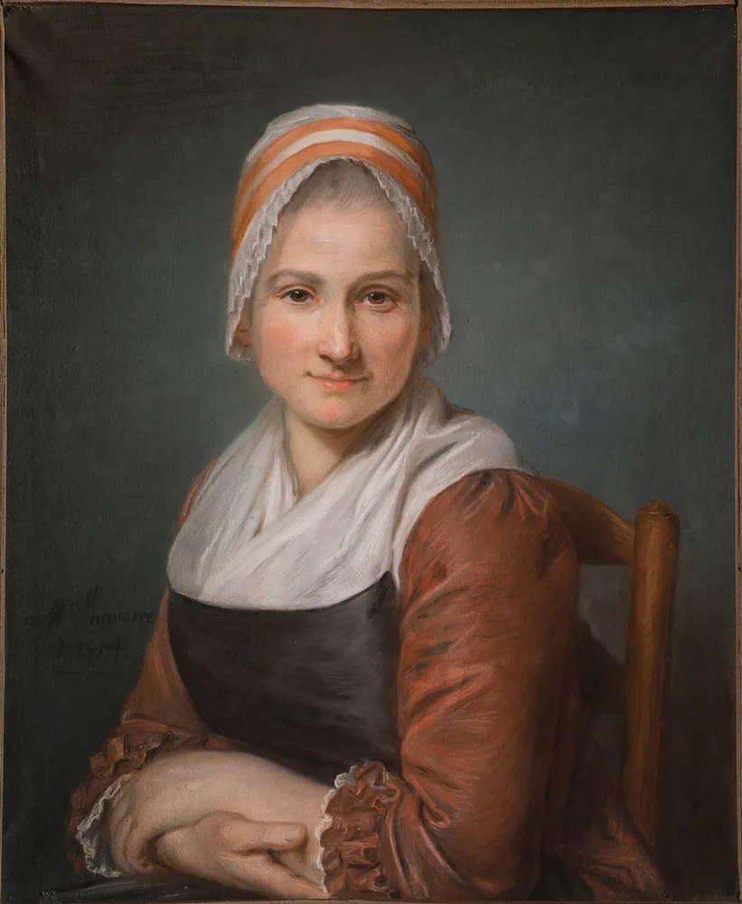 A light-skinned woman with a direct and calm expression sits in a wooden chair, looking straight at the viewer. She wears a dress with red sleeves and a white kerchief that tucks into a blue bodice. Her hair is covered in a white and orange cap that frames her face with lace.