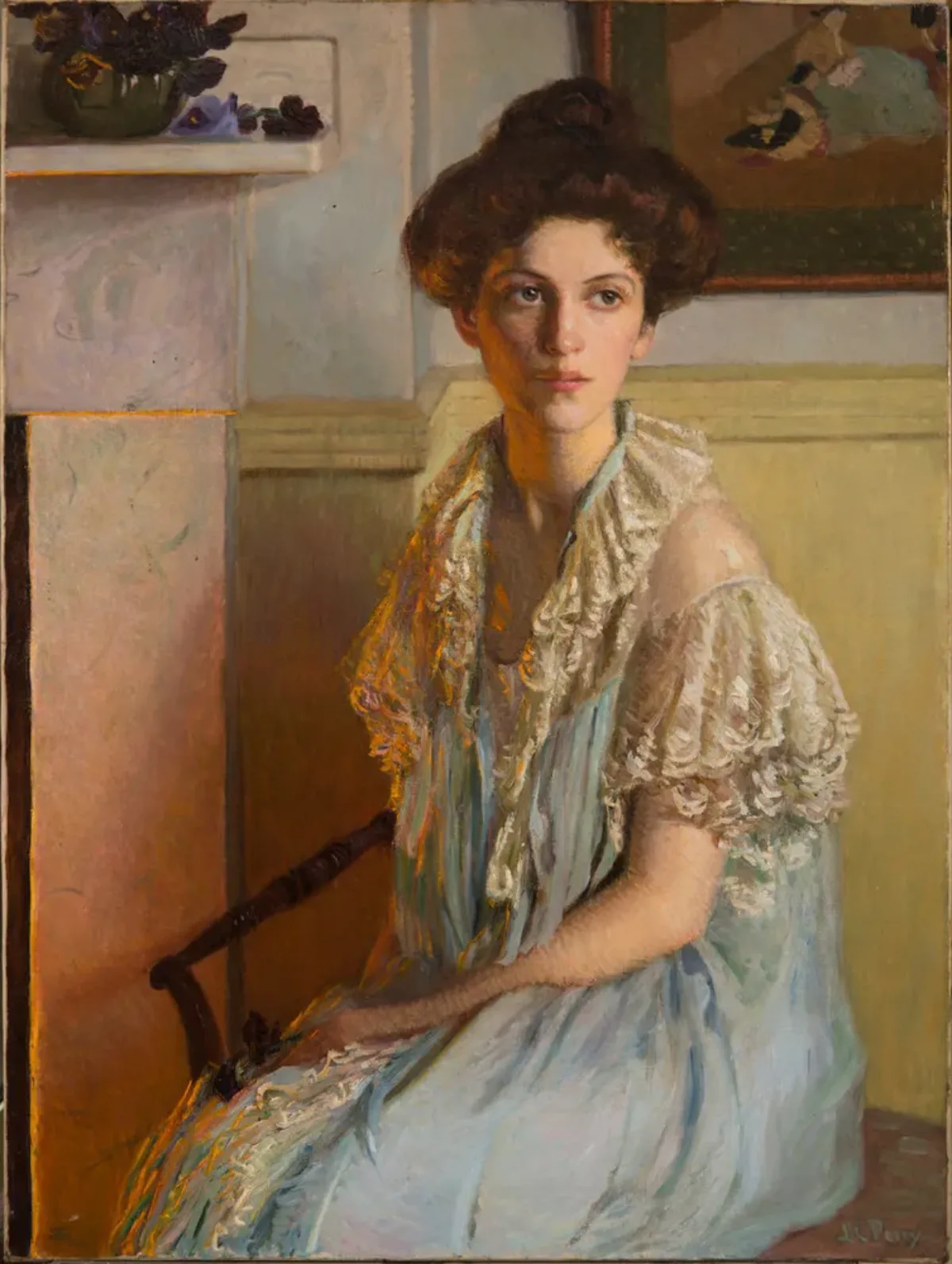 A young woman sits on a chair with her hair in a loose bun, wearing a white lace-trim gown. Her body turns slightly right towards a fireplace, its orange glow reflected on her hair and torso. The room is light and clean and a dark bowl overflowing with violets sits on the mantle.