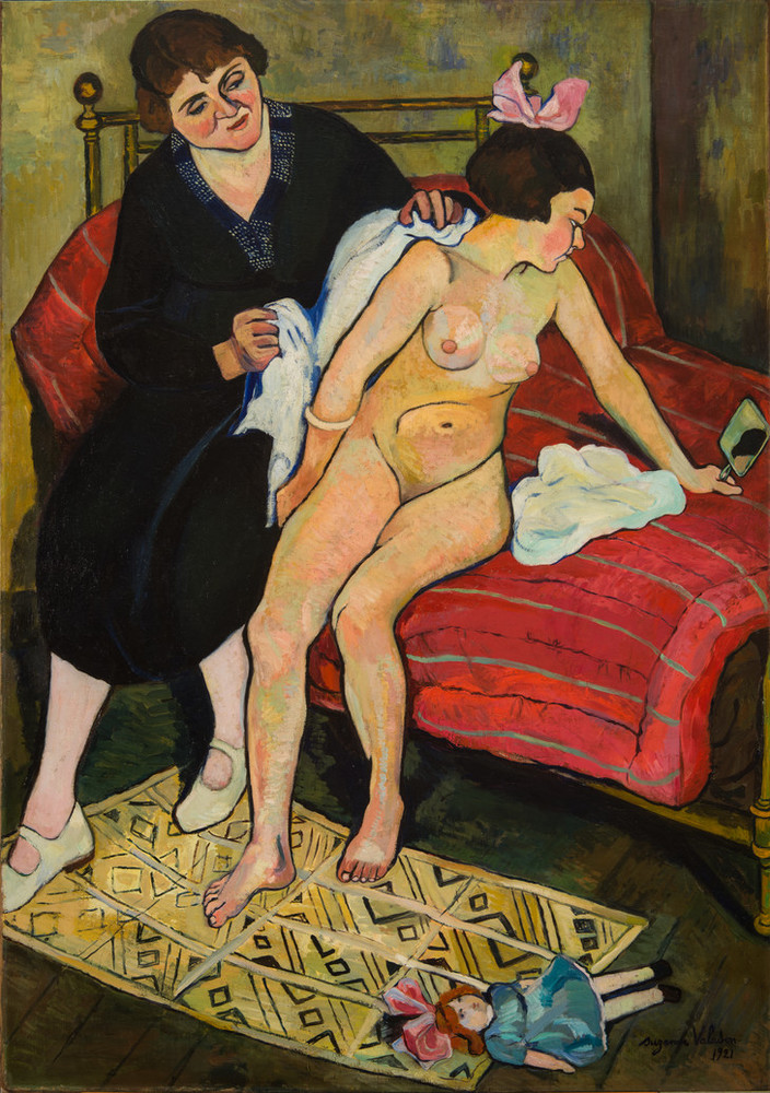 Seated on a bed, a fully clothed woman with light skin dries off a naked adolescent girl. The girl, wearing only a pink hair ribbon, turns away from the woman and inspects herself in a handheld mirror.