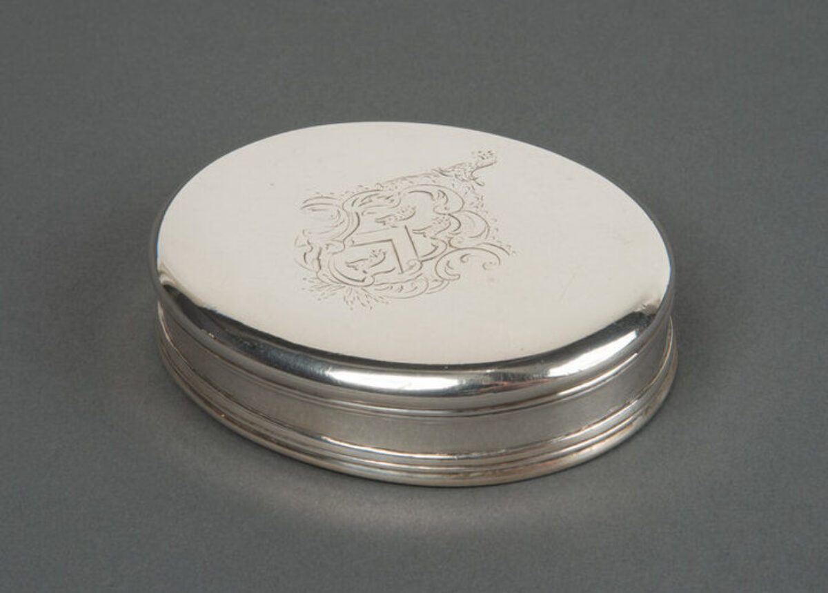 Small oval tobacco box made of silver. The relatively plain box features a Rococo engraving of a coat of arms at the center of the lid.