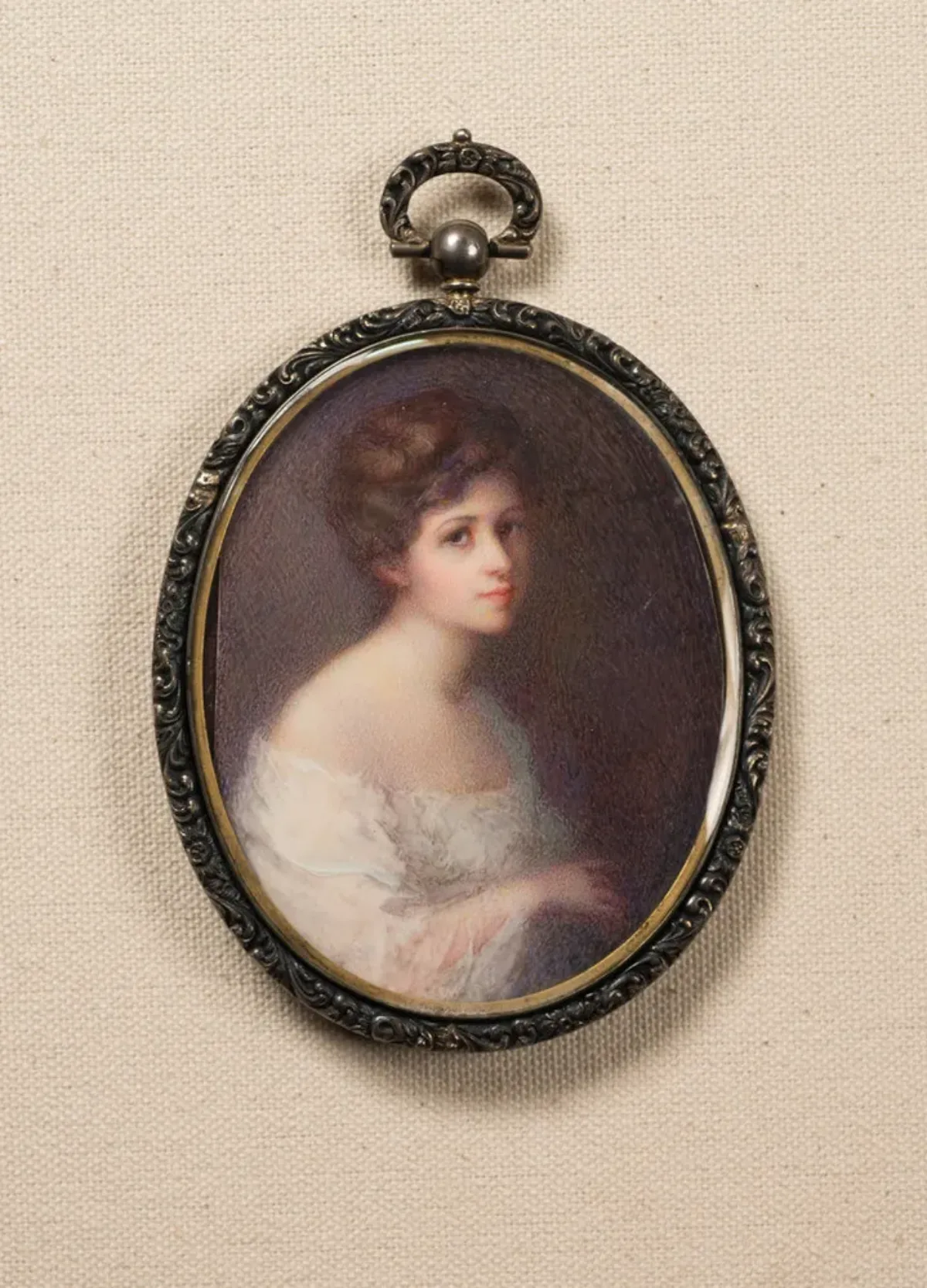 A softly painted, miniature self-portrait in an oval frame portrays the light-skinned, brunette artist against a dark background. Clad in a white, off-the-shoulder gauzy garment, she appears from the waist up, her body facing right. She turns her gaze toward the viewer.